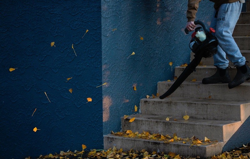 mężczyzna używa dmuchawy ogrodowej, aby usunąć liście ze schodów